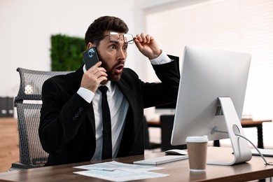 Photo of Man talking on smartphone while working at table in office