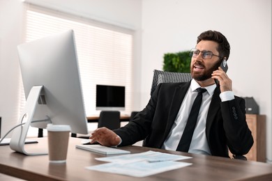 Photo of Man talking on smartphone while working at table in office