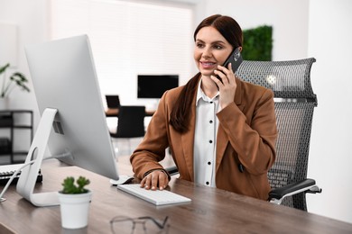 Photo of Woman talking on smartphone while working at table in office