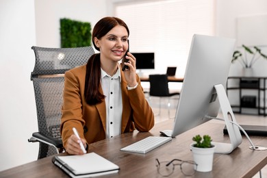 Photo of Woman talking on smartphone while working at table in office