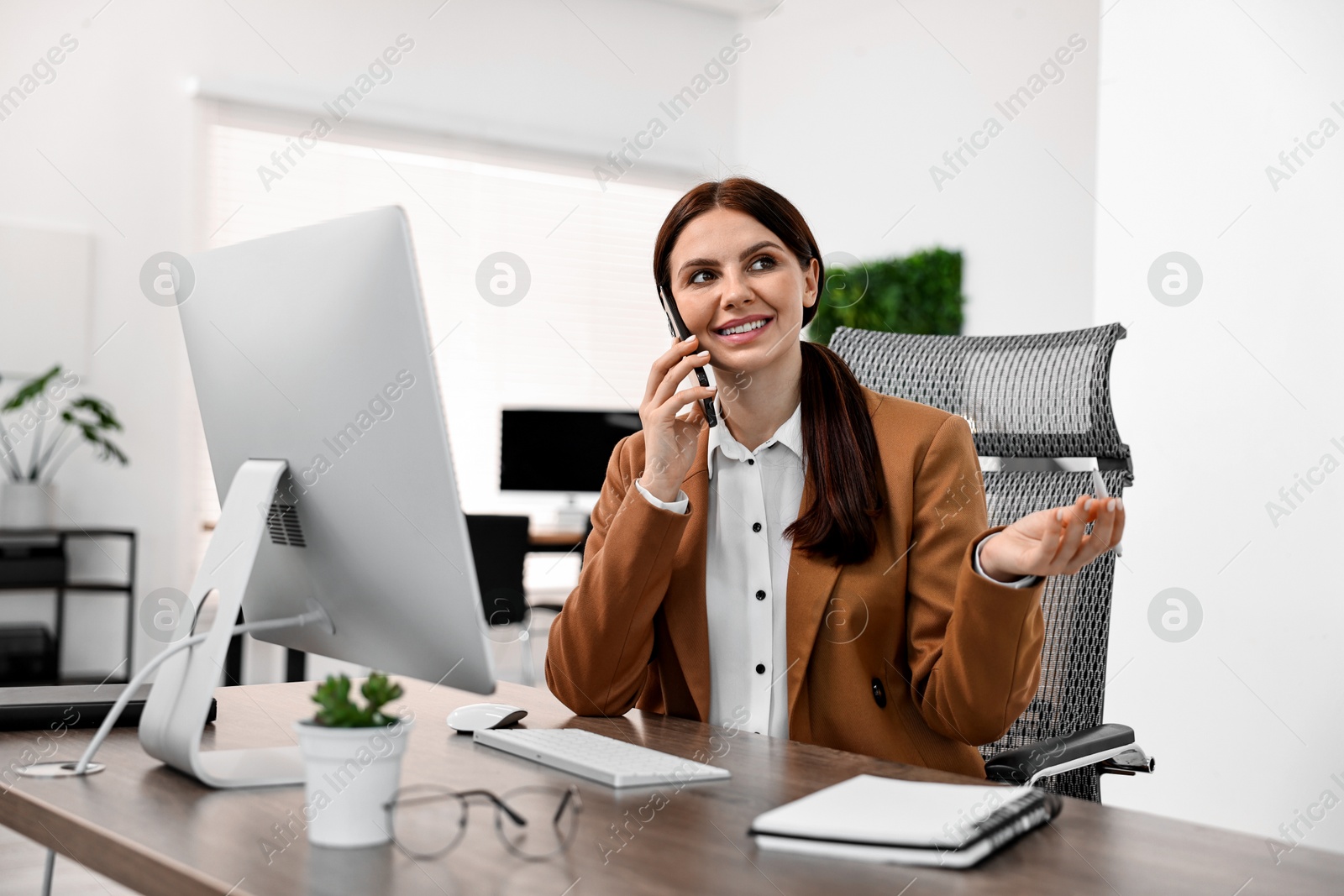 Photo of Woman talking on smartphone while working at table in office