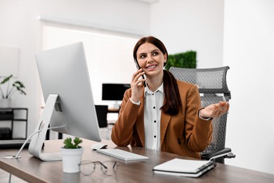 Photo of Woman talking on smartphone while working at table in office