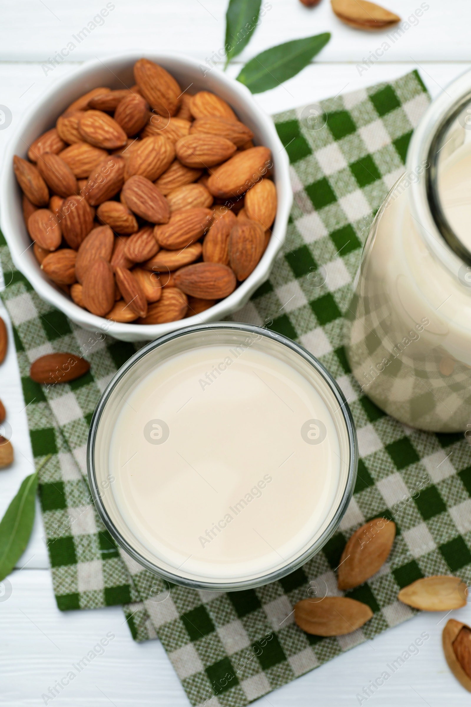 Photo of Fresh nut milk, almonds and green leaves on white wooden table, flat lay