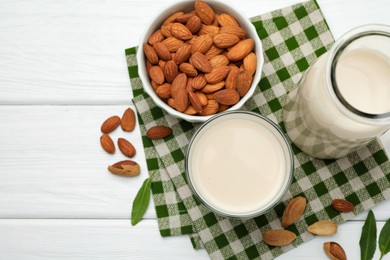 Fresh nut milk, almonds and green leaves on white wooden table, flat lay. Space for text