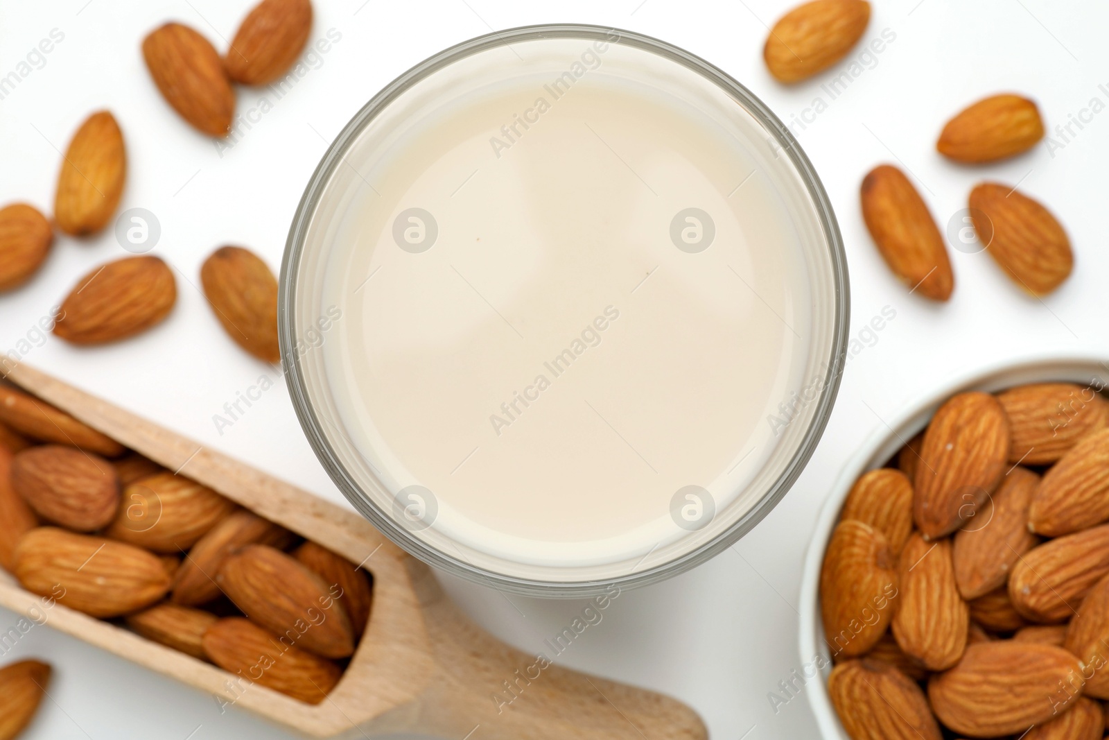 Photo of Fresh nut milk in glass and almonds on white table, flat lay