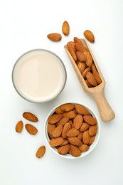 Fresh nut milk in glass and almonds on white table, flat lay