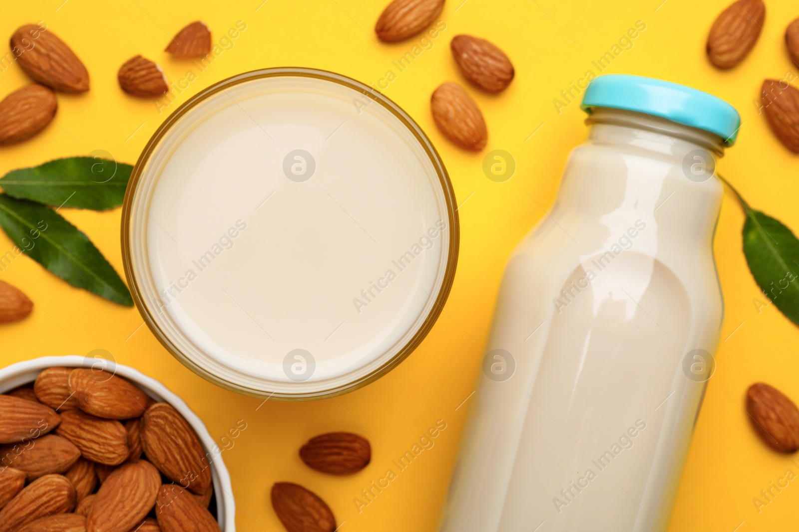 Photo of Fresh nut milk, almonds and green leaves on yellow background, flat lay