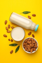 Fresh nut milk, almonds and green leaves on yellow background, flat lay