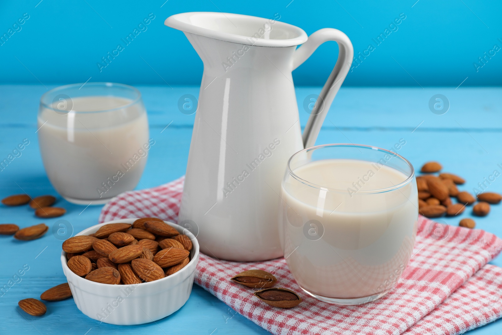 Photo of Fresh nut milk and almonds on light blue wooden table