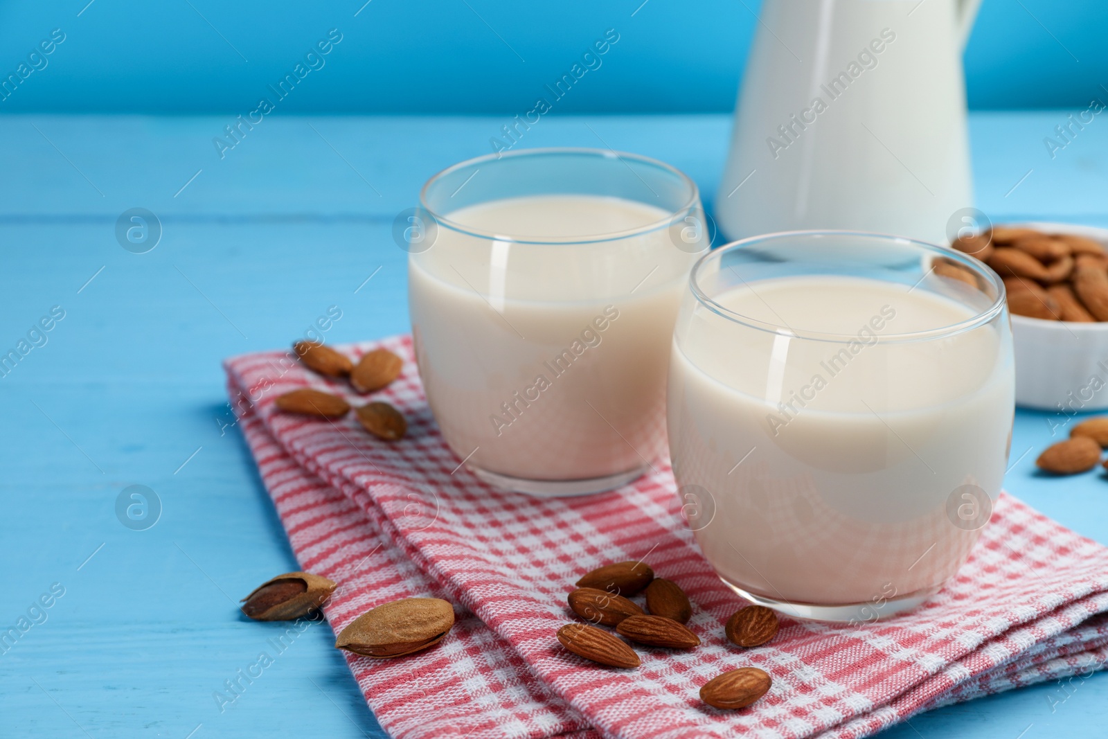 Photo of Fresh nut milk in glasses and almonds on light blue wooden table, closeup