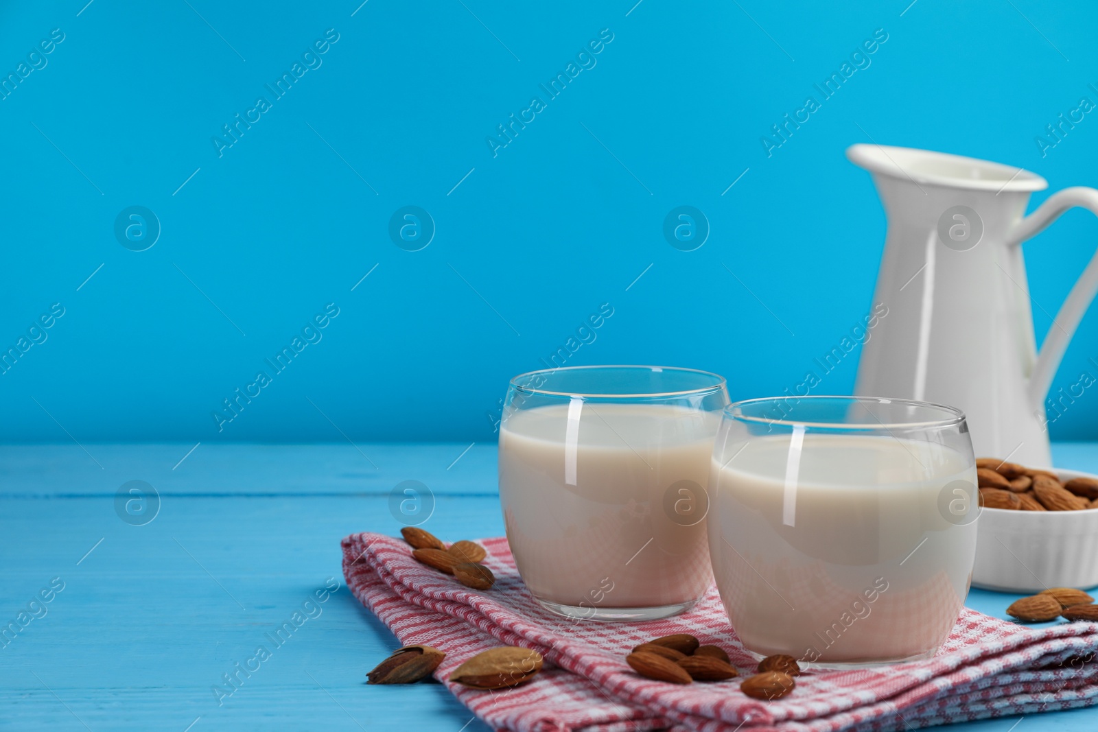 Photo of Fresh nut milk and almonds on light blue wooden table, space for text