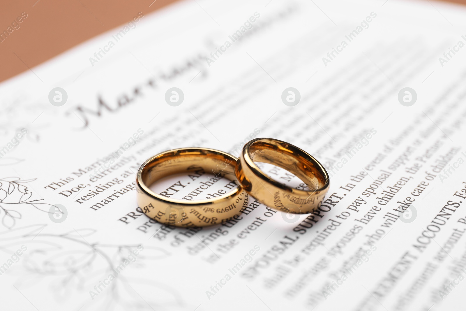 Photo of Marriage contract and golden rings on brown background, closeup