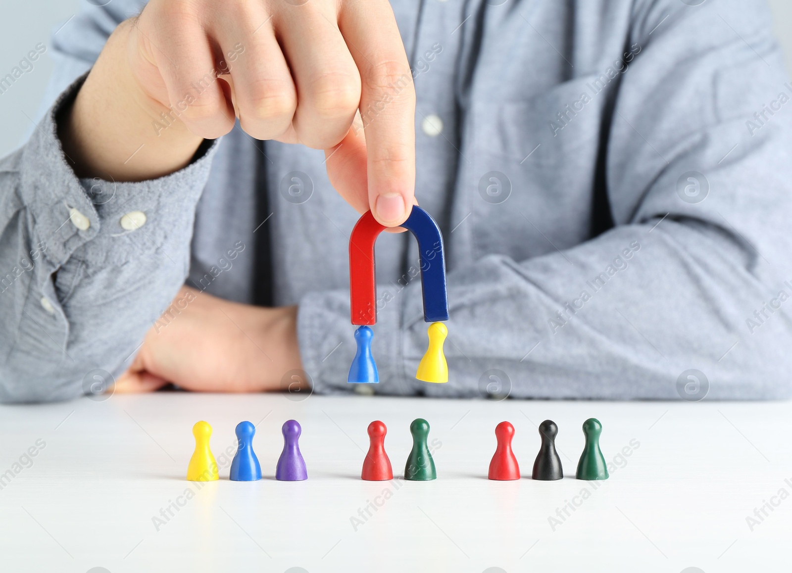 Photo of Man with magnet attracting game pieces at white table, closeup