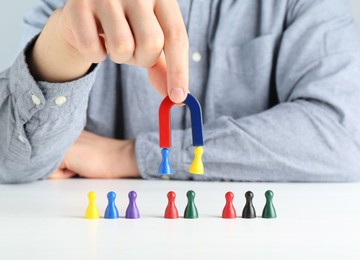 Photo of Man with magnet attracting game pieces at white table, closeup