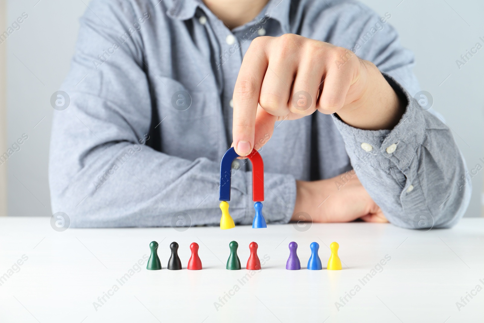 Photo of Man with magnet attracting game pieces at white table, closeup