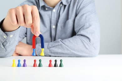 Photo of Man with magnet attracting game pieces at white table, closeup