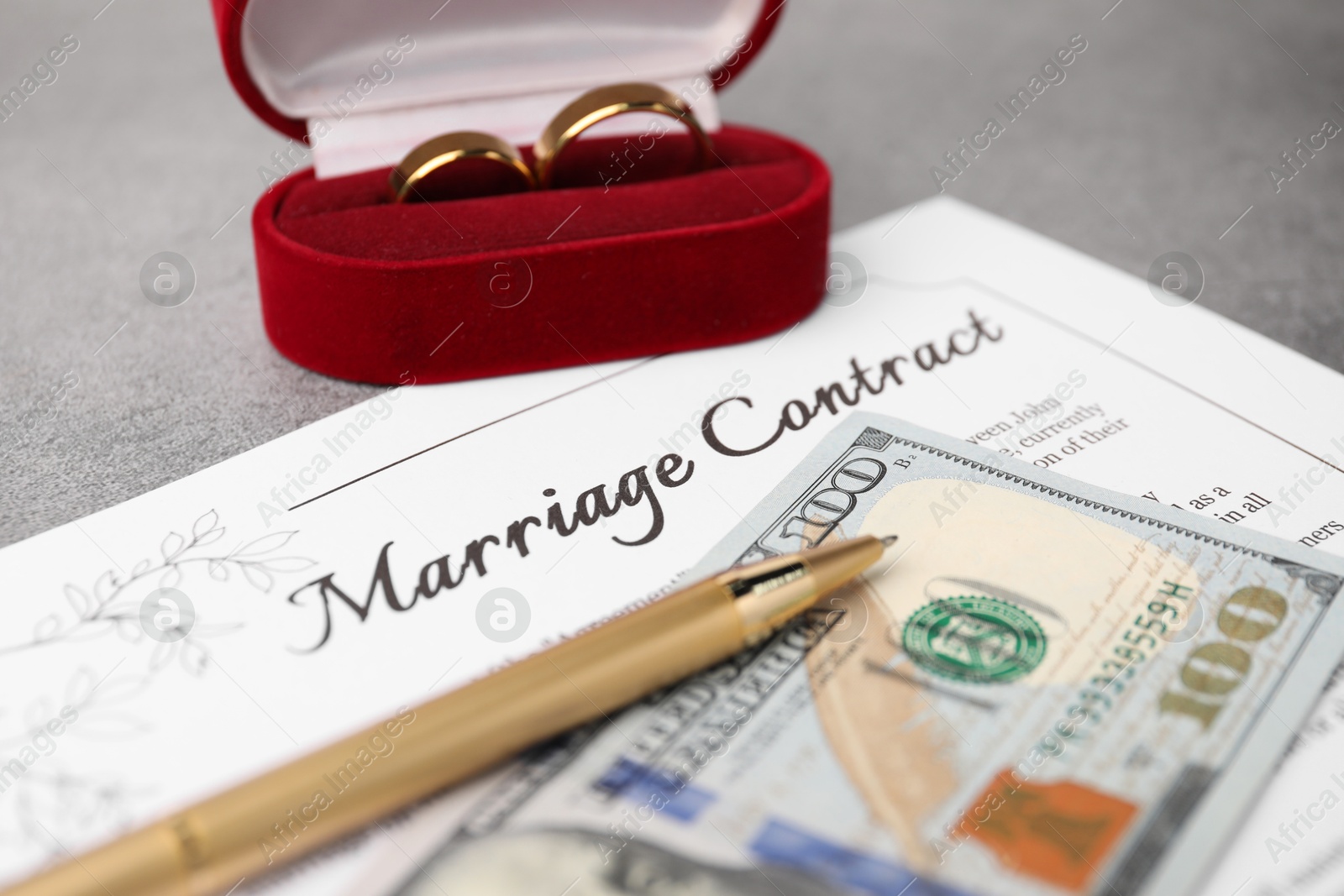 Photo of Marriage contract, pen, dollar bill and golden rings on grey table, closeup