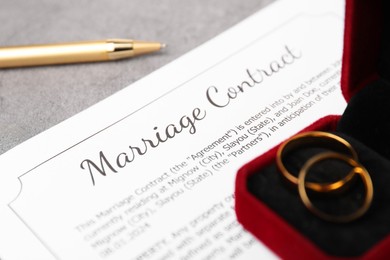 Photo of Marriage contract, pen and golden rings on grey table, closeup