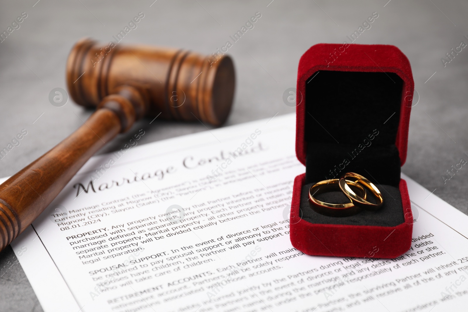 Photo of Marriage contract, gavel and golden rings on grey table, closeup