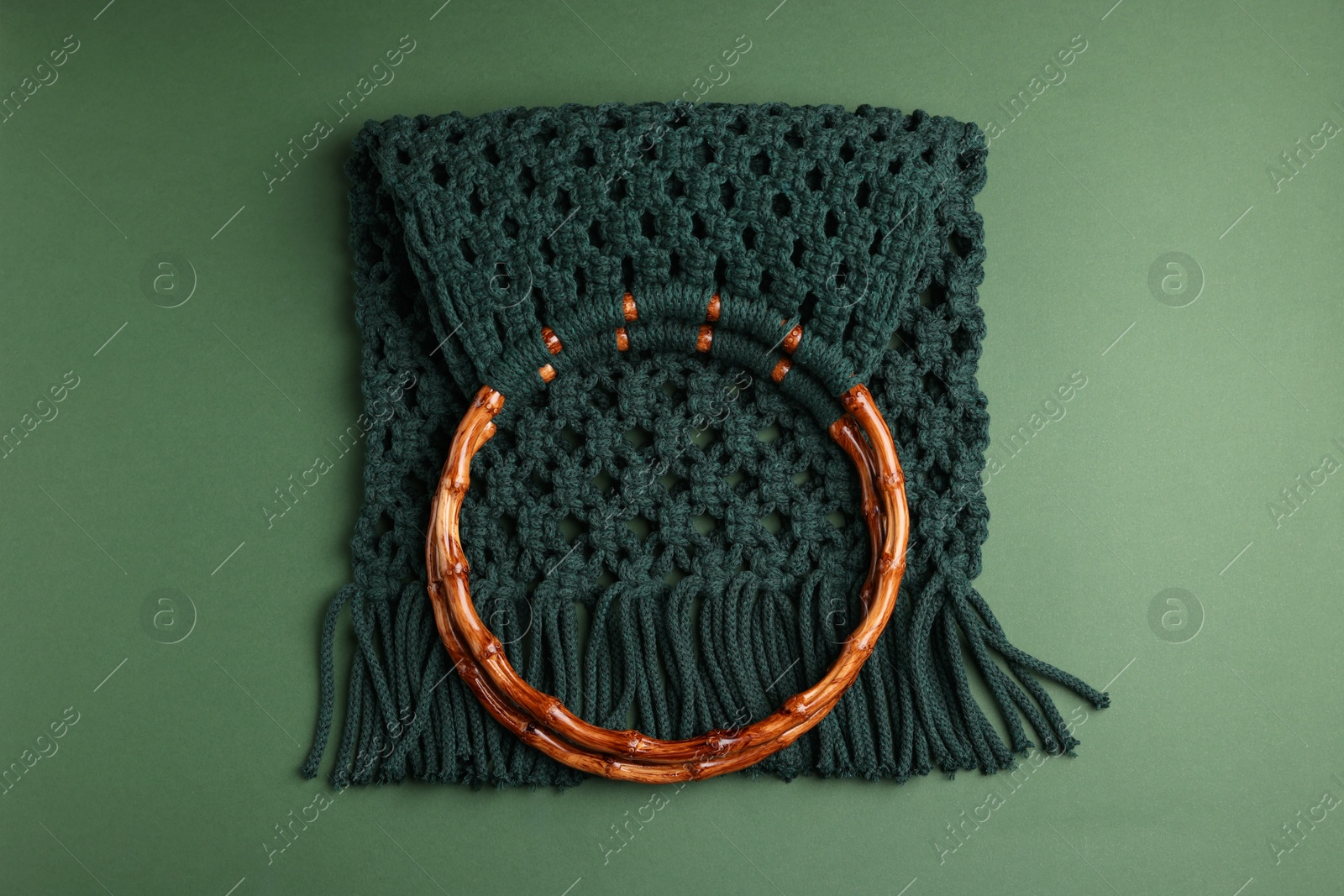 Photo of Macrame shopping bag with wooden handles on green background, top view