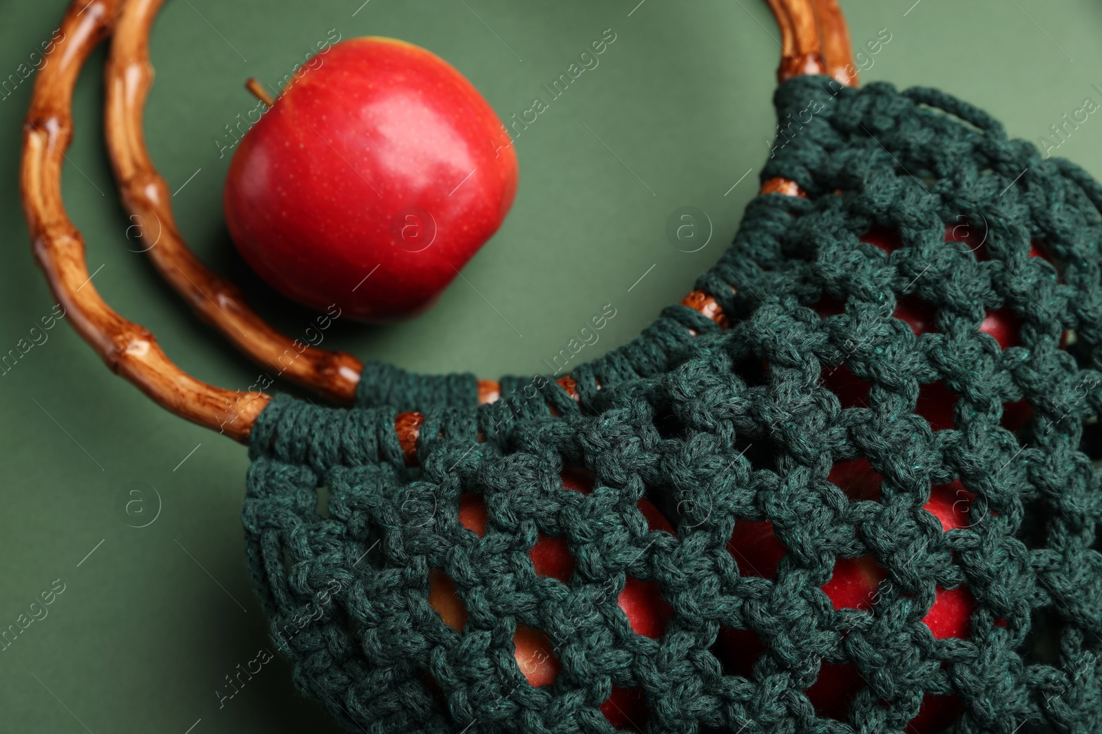 Photo of Macrame shopping bag with wooden handles and apple on green background, closeup