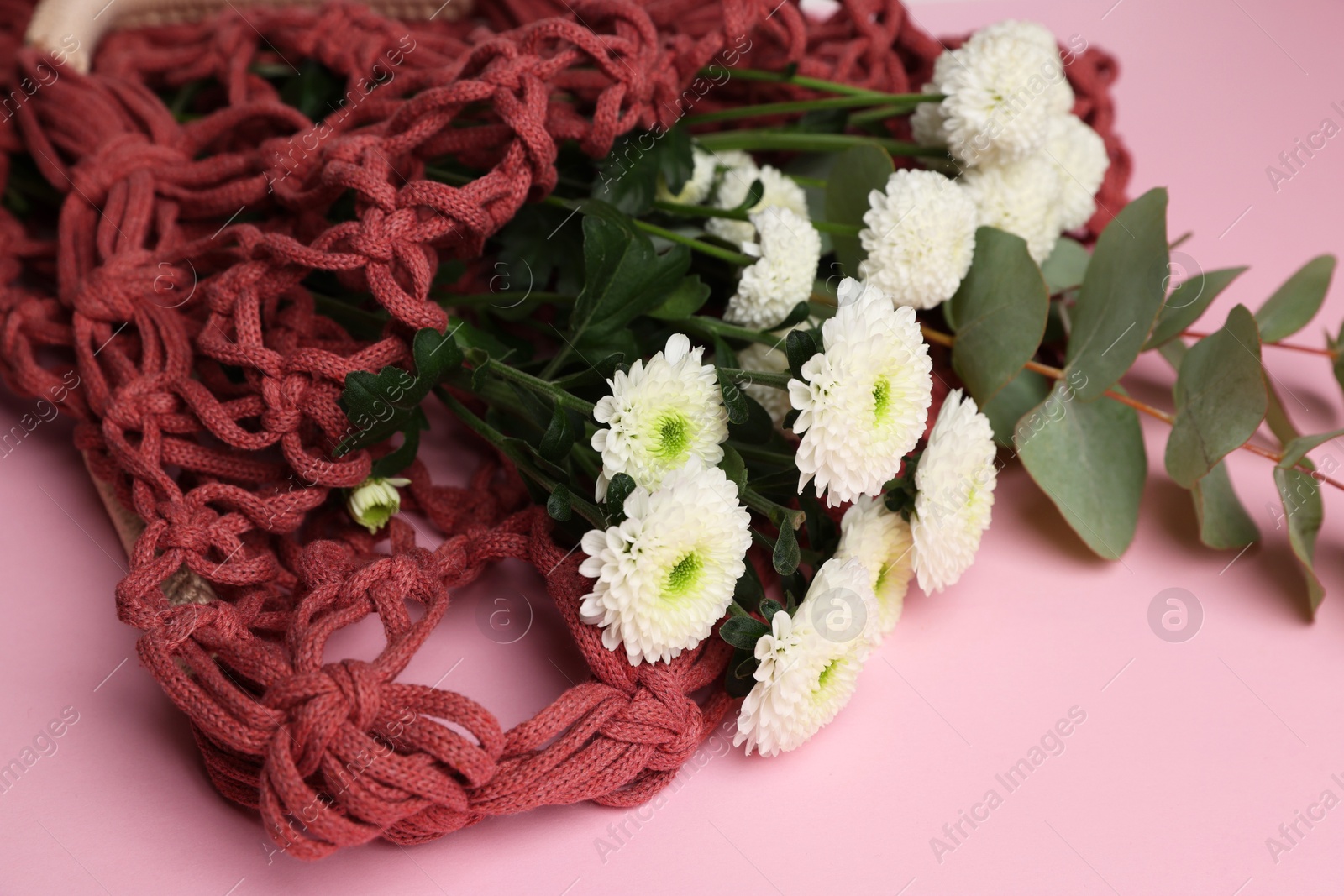 Photo of Macrame shopping bag with flowers and eucalyptus branch on pink background, closeup