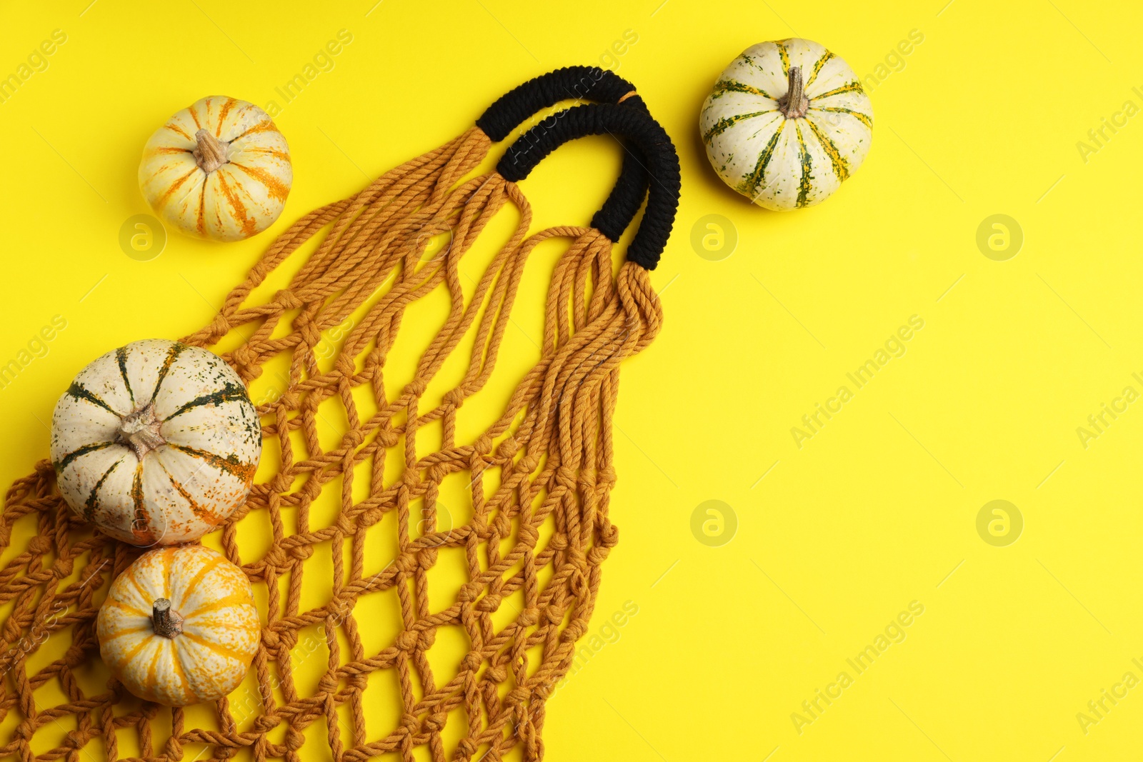 Photo of Macrame shopping bag and pumpkins on yellow background, flat lay. Space for text