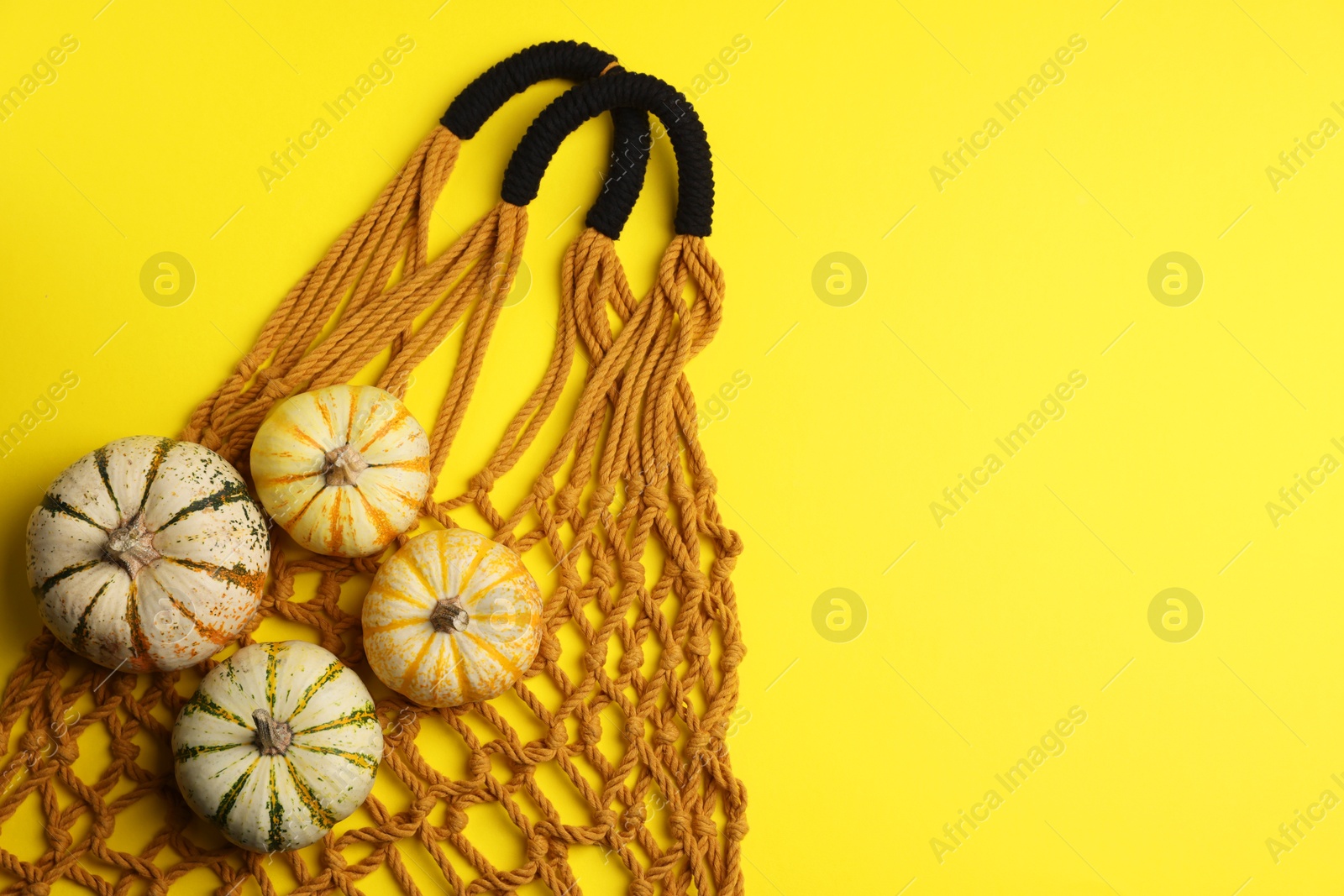 Photo of Macrame shopping bag and pumpkins on yellow background, top view. Space for text