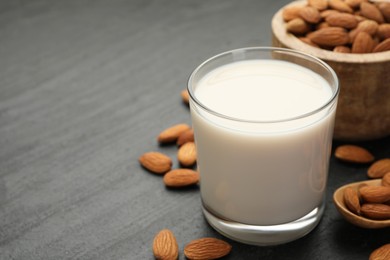 Photo of Fresh almond milk in glass, spoon and nuts on black table, closeup. Space for text