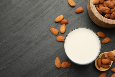 Fresh almond milk in glass, spoon and nuts on black table, top view. Space for text