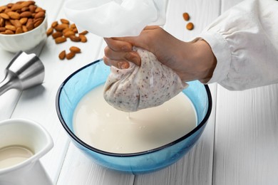 Woman making almond milk and nuts at white wooden table, closeup