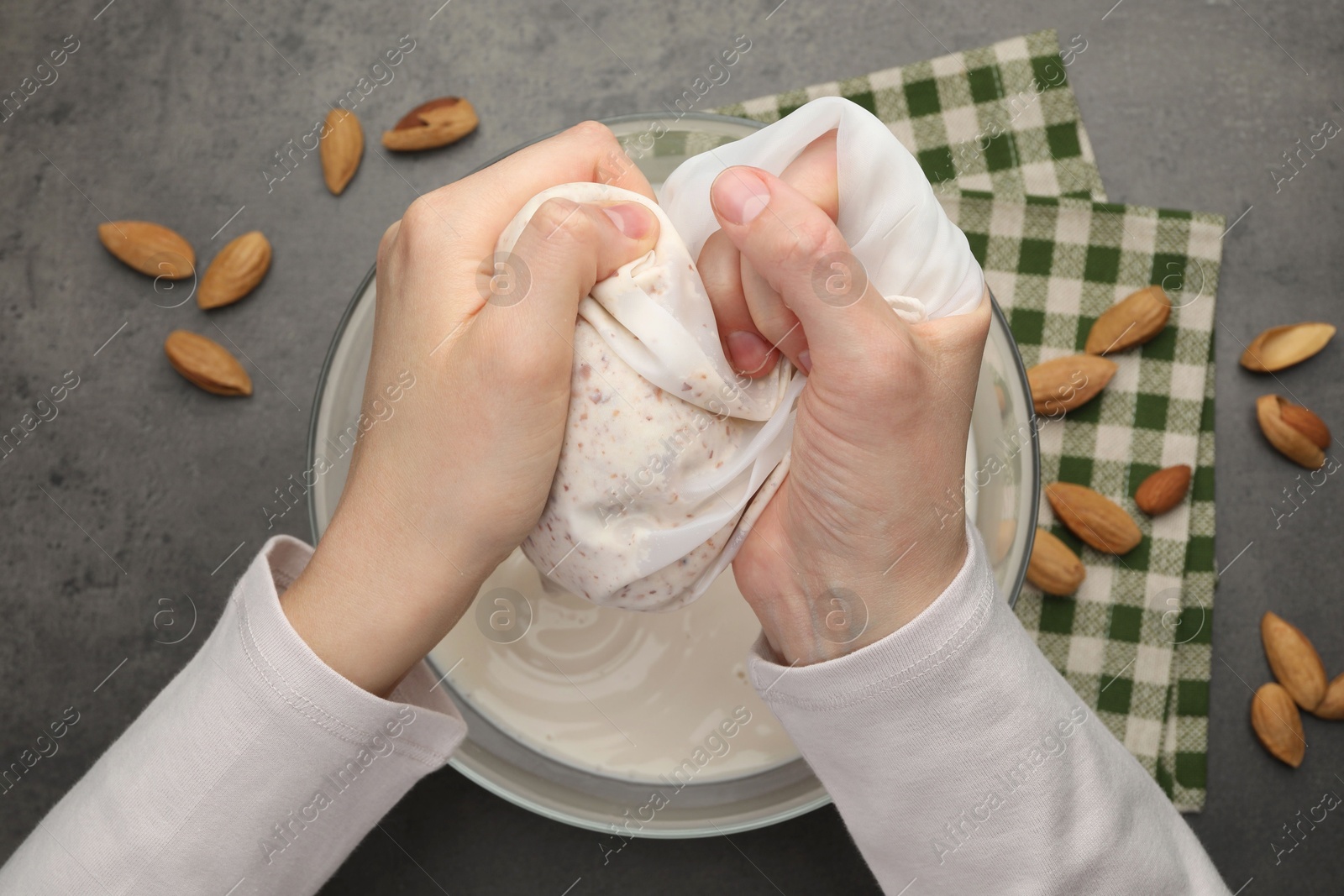 Photo of Woman making almond milk and nuts at black table, top view