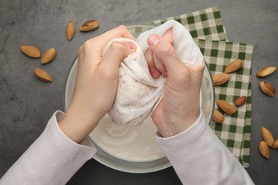 Woman making almond milk and nuts at black table, top view