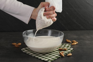 Woman making almond milk and nuts at black table, closeup