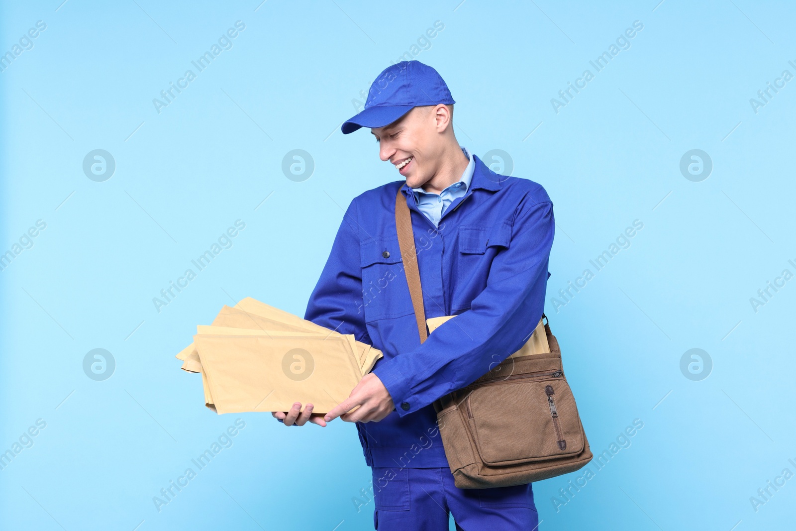 Photo of Happy postman with bag and envelopes on light blue background