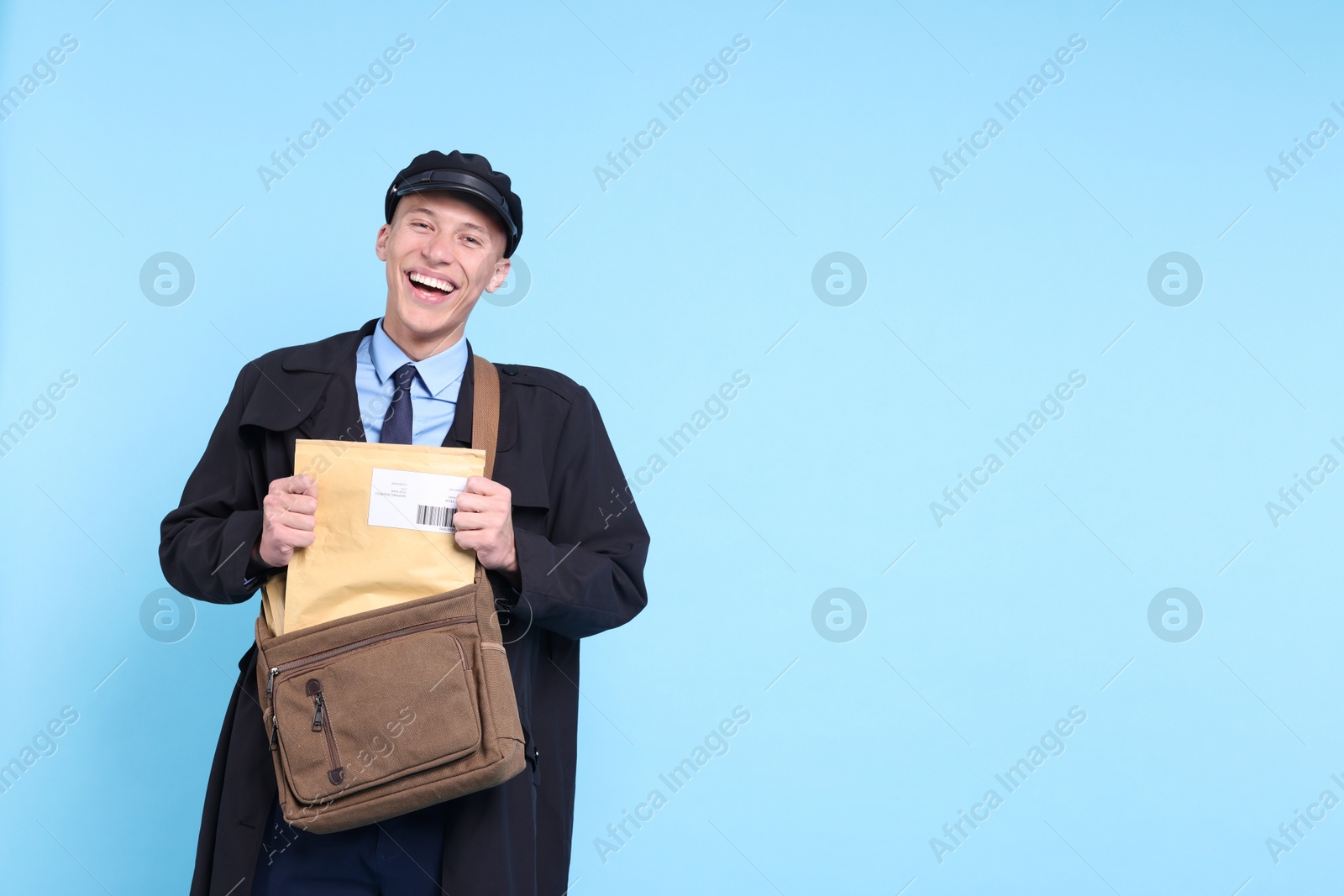 Photo of Happy postman with bag and envelopes on light blue background. Space for text