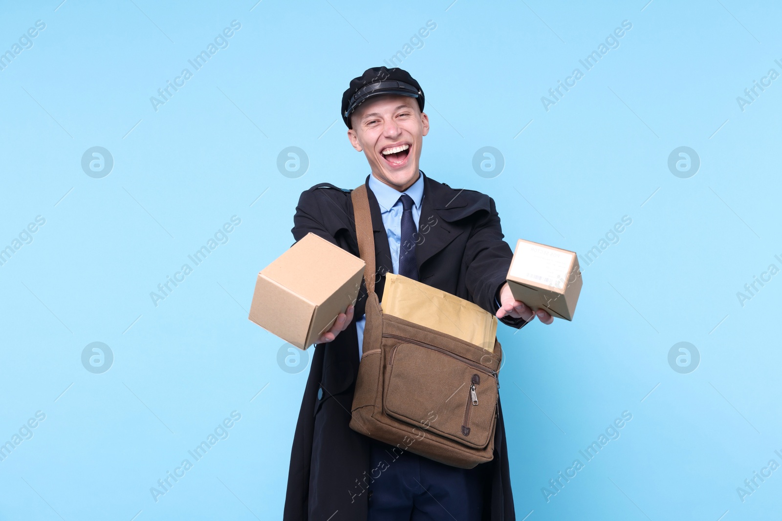 Photo of Happy postman with bag giving parcels on light blue background