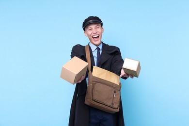 Photo of Happy postman with bag giving parcels on light blue background