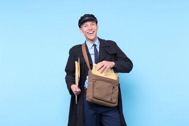 Photo of Happy postman with bag and envelopes on light blue background