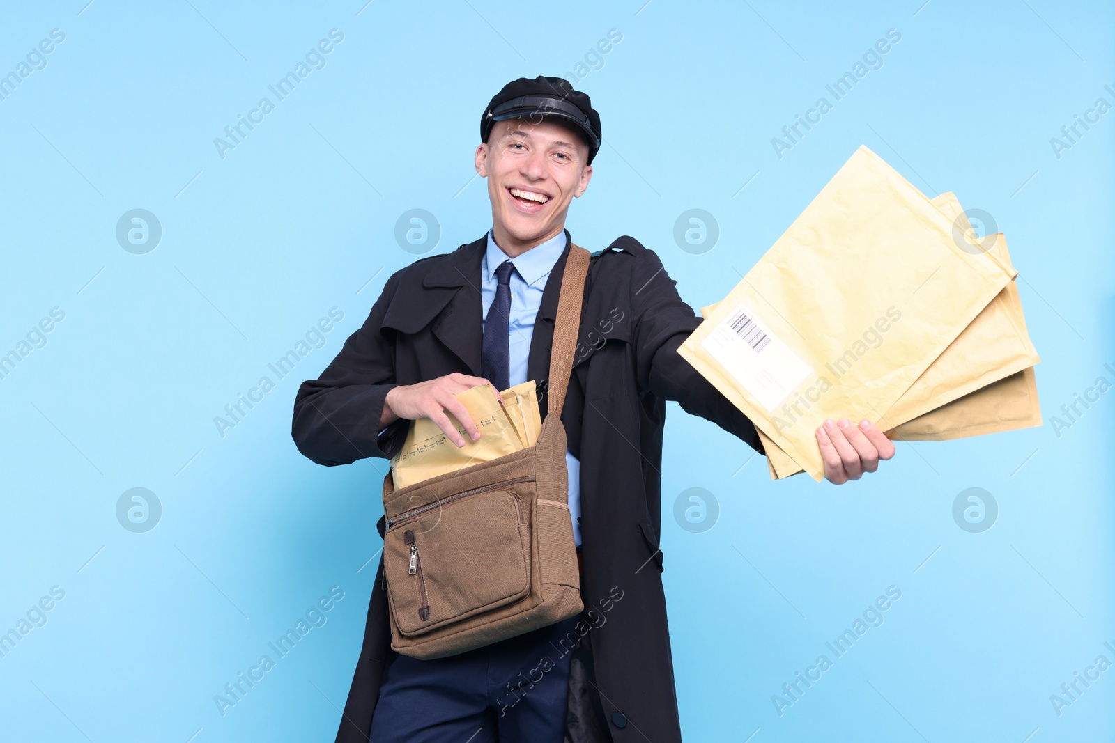 Photo of Happy postman with bag giving envelopes on light blue background