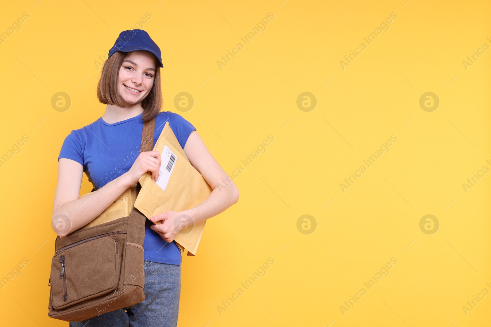 Photo of Happy postwoman with bag and envelopes on yellow background. Space for text