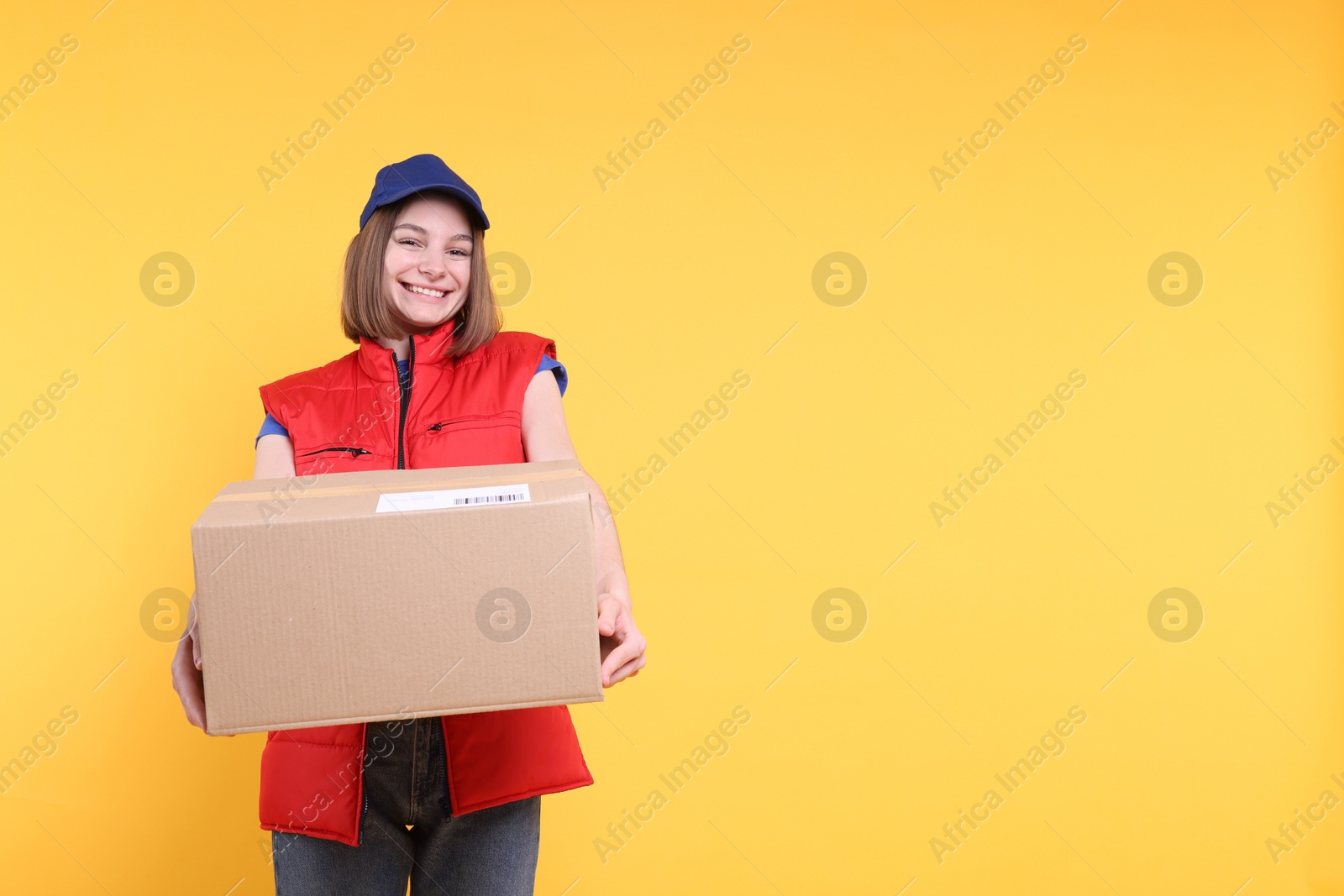 Photo of Happy postwoman giving parcel on yellow background. Space for text