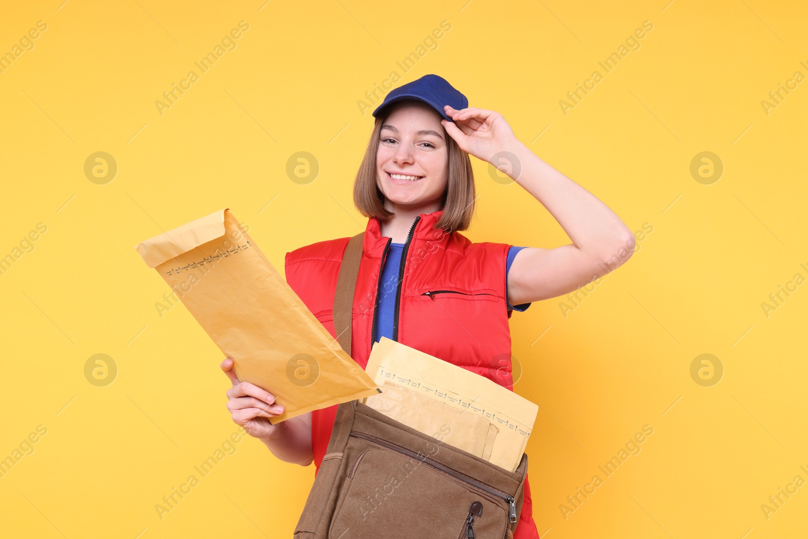 Photo of Happy postwoman with bag and envelopes on yellow background