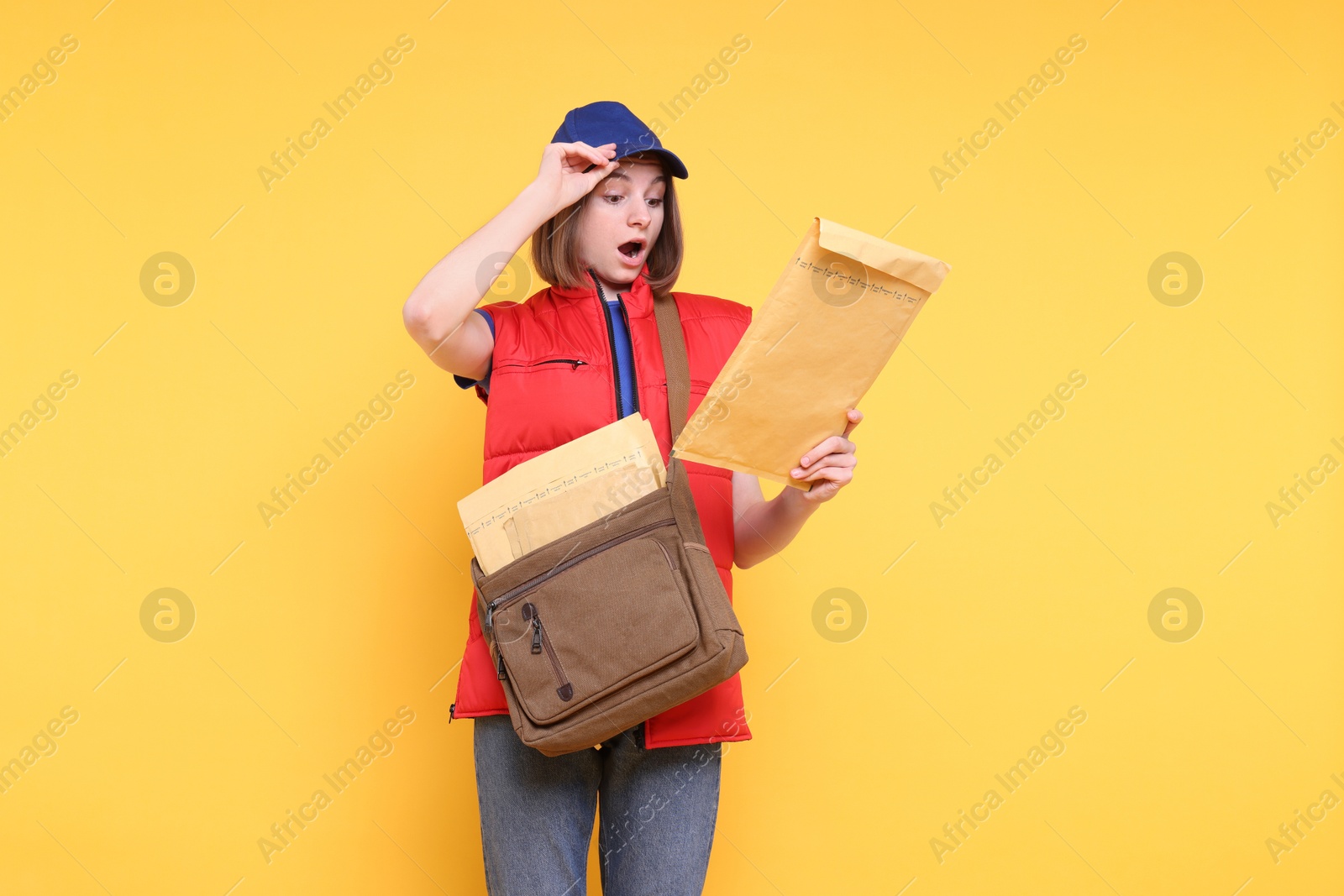 Photo of Surprised postwoman with bag and envelopes on yellow background