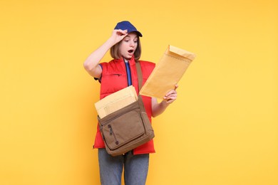 Photo of Surprised postwoman with bag and envelopes on yellow background