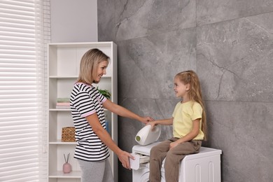 Photo of Housewife and her daughter doing laundry together indoors