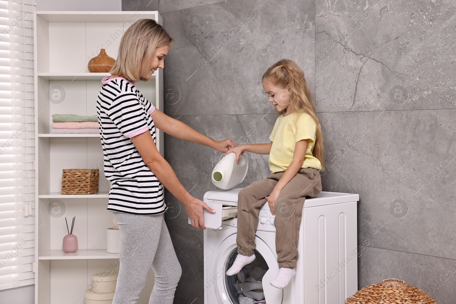 Photo of Housewife and her daughter doing laundry together indoors