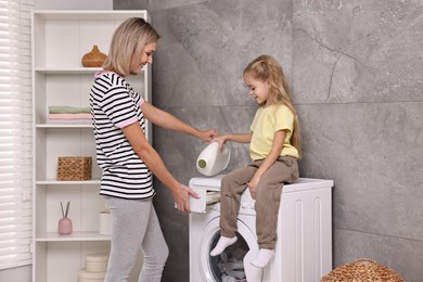 Photo of Housewife and her daughter doing laundry together indoors