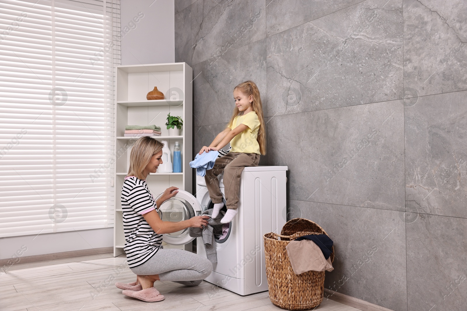 Photo of Housewife and her daughter doing laundry together indoors