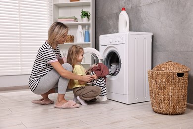 Photo of Housewife and her daughter doing laundry together indoors